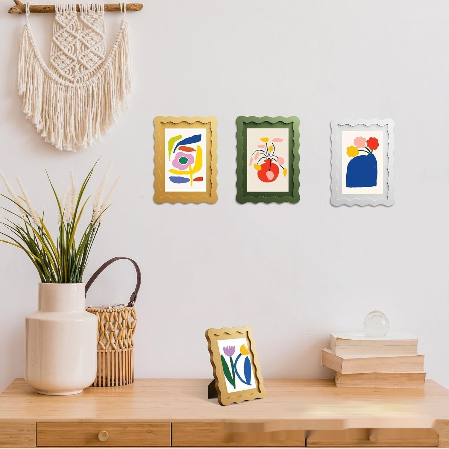 Decorative wall with framed abstract art, plants, and books on a wooden surface.