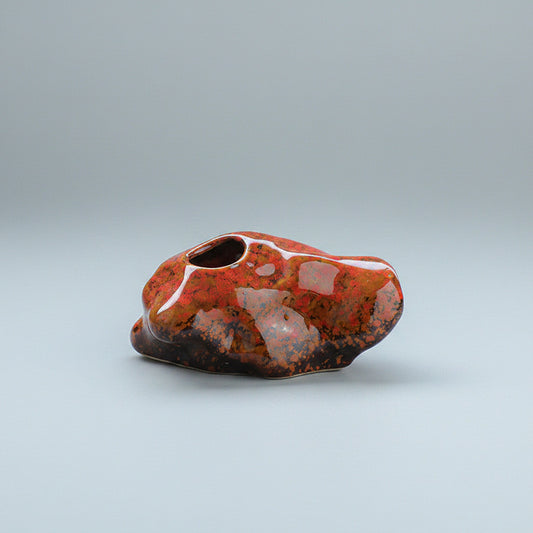 Red ceramic object on a table with a blue and white patterned cup in the background