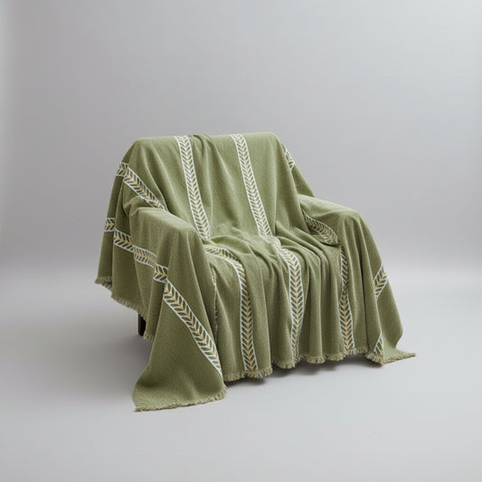 Green blanket with white patterns draped over a couch in a room with a window and green curtain.